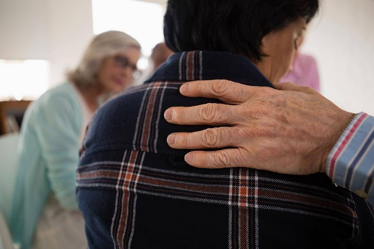 Eine Hand liegt tröstend auf der Schulter einer Person, die man von hinten sieht