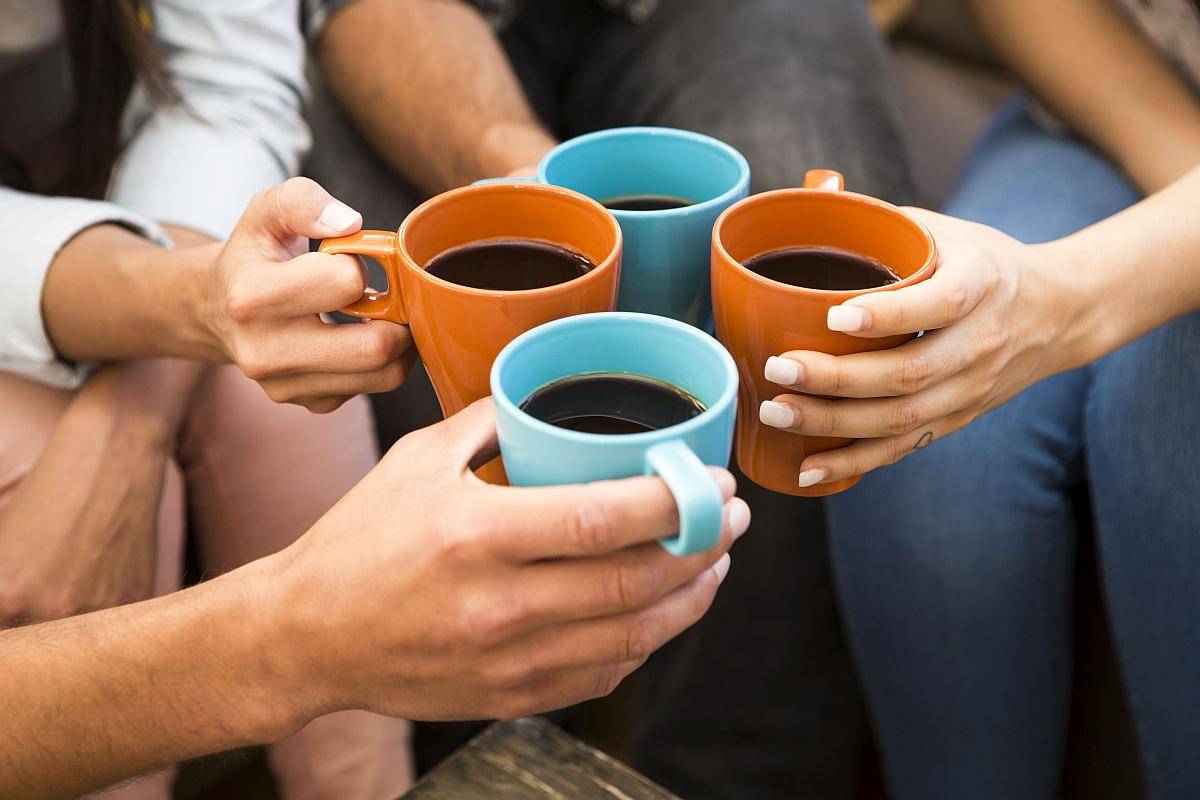 Menschen sitzen in einer Runde da und halten Kaffeetassen in der Hand