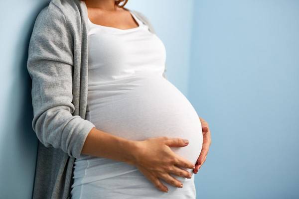 Eine schwangere Frau umfasst ihren Babybauch mit beiden Händen