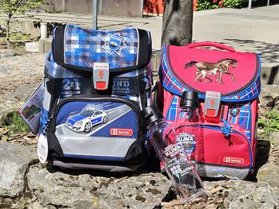 Zwei Schulranzen stehen nebeneinander auf einer Mauer